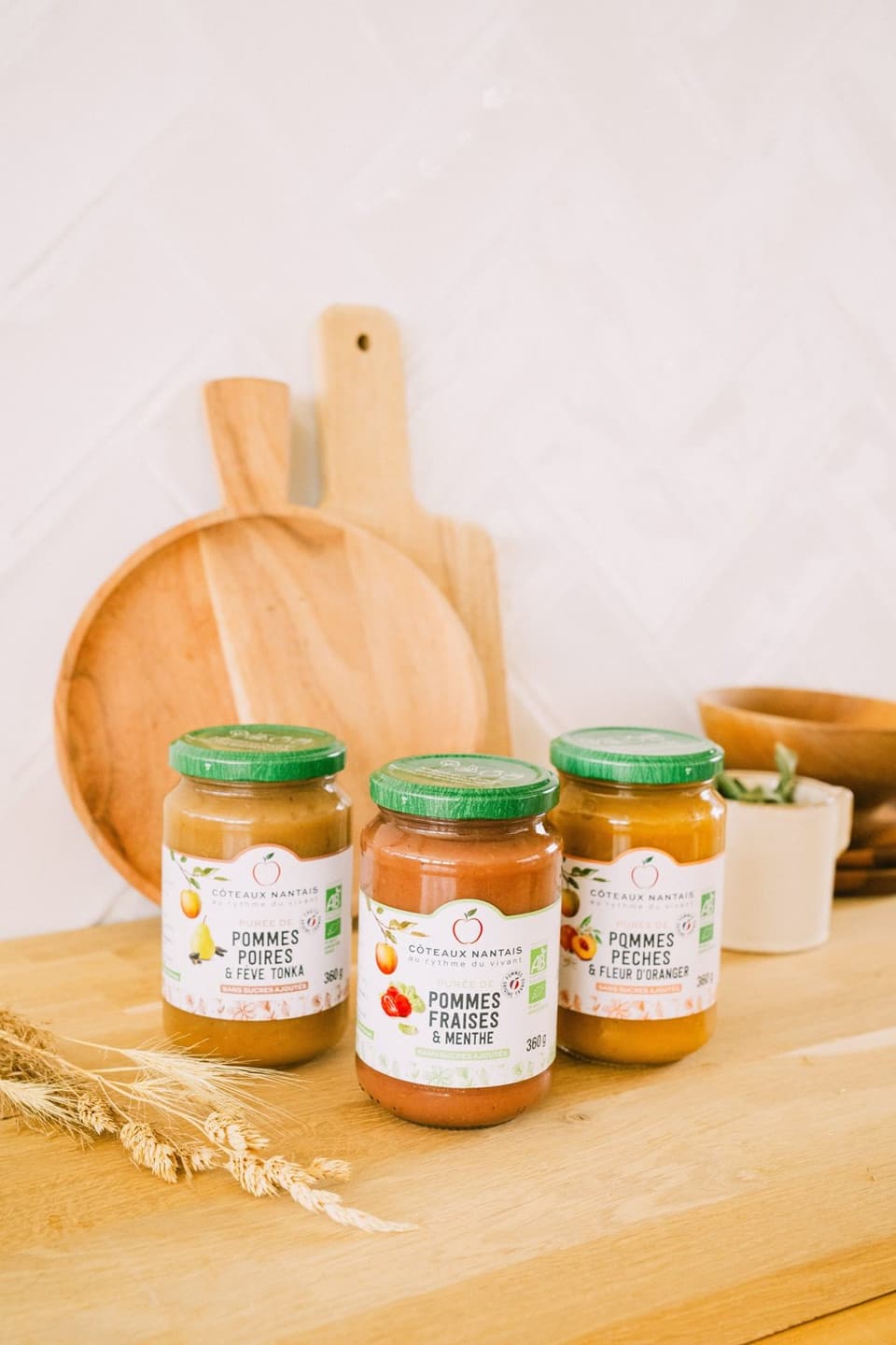 Three jars of compote, apple-pear, apple-strawberry and apple-peach, on a wooden board